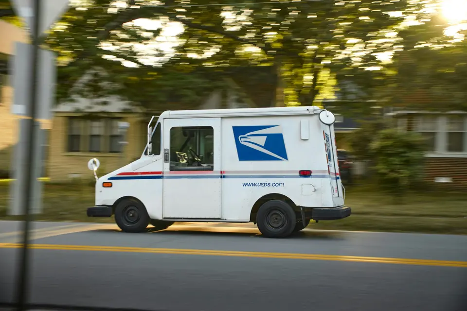 Hvit amerikansk postbil kjører langs en boliggate